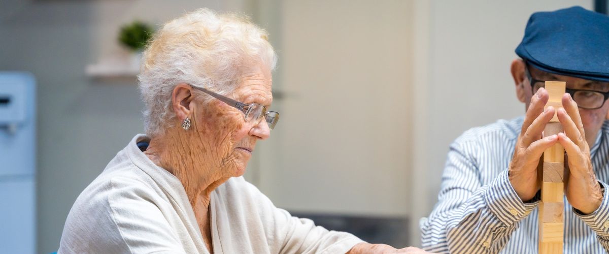 An older woman stacks wooden blocks at a table during a day program.